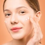 Young woman applying facial cream for healthy skincare routine.