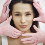 Close-up of a woman receiving a skincare treatment with pink gloves indoors.