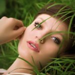 Close-up of a woman lying in lush green grass with a serene expression.