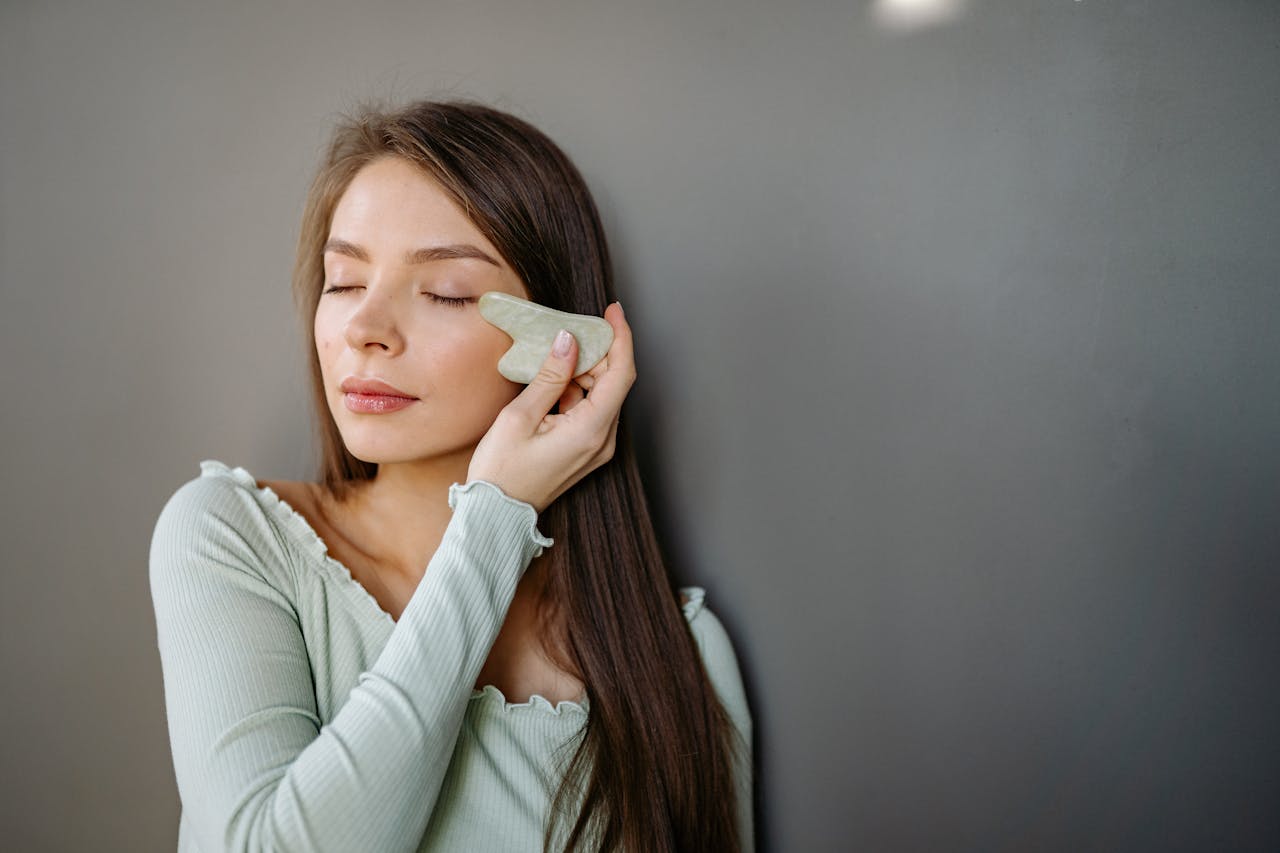 Woman using jade stone for Gua Sha massage, promoting relaxation and skincare.