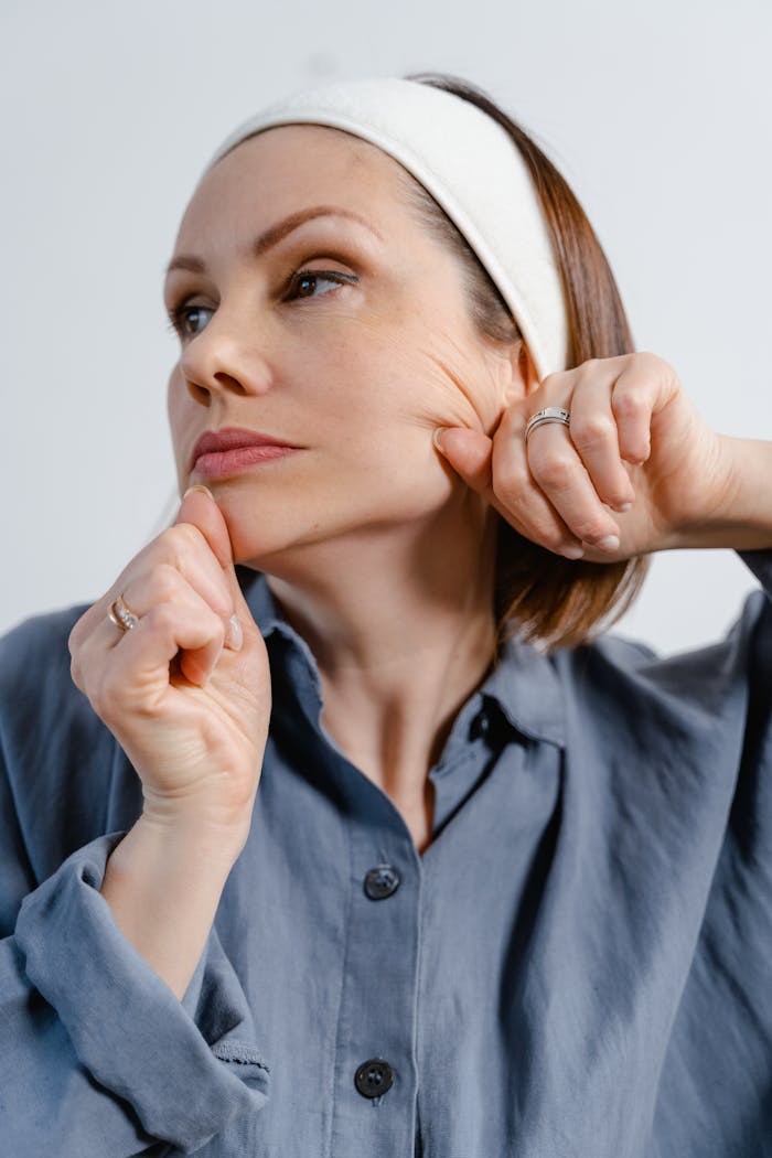A woman practices skincare facial massage wearing a white headband in a studio setting.